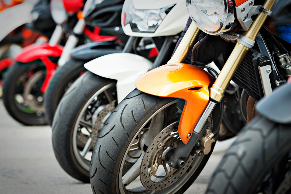 Row of motorcycles parked, focus on orange front fender and tire.