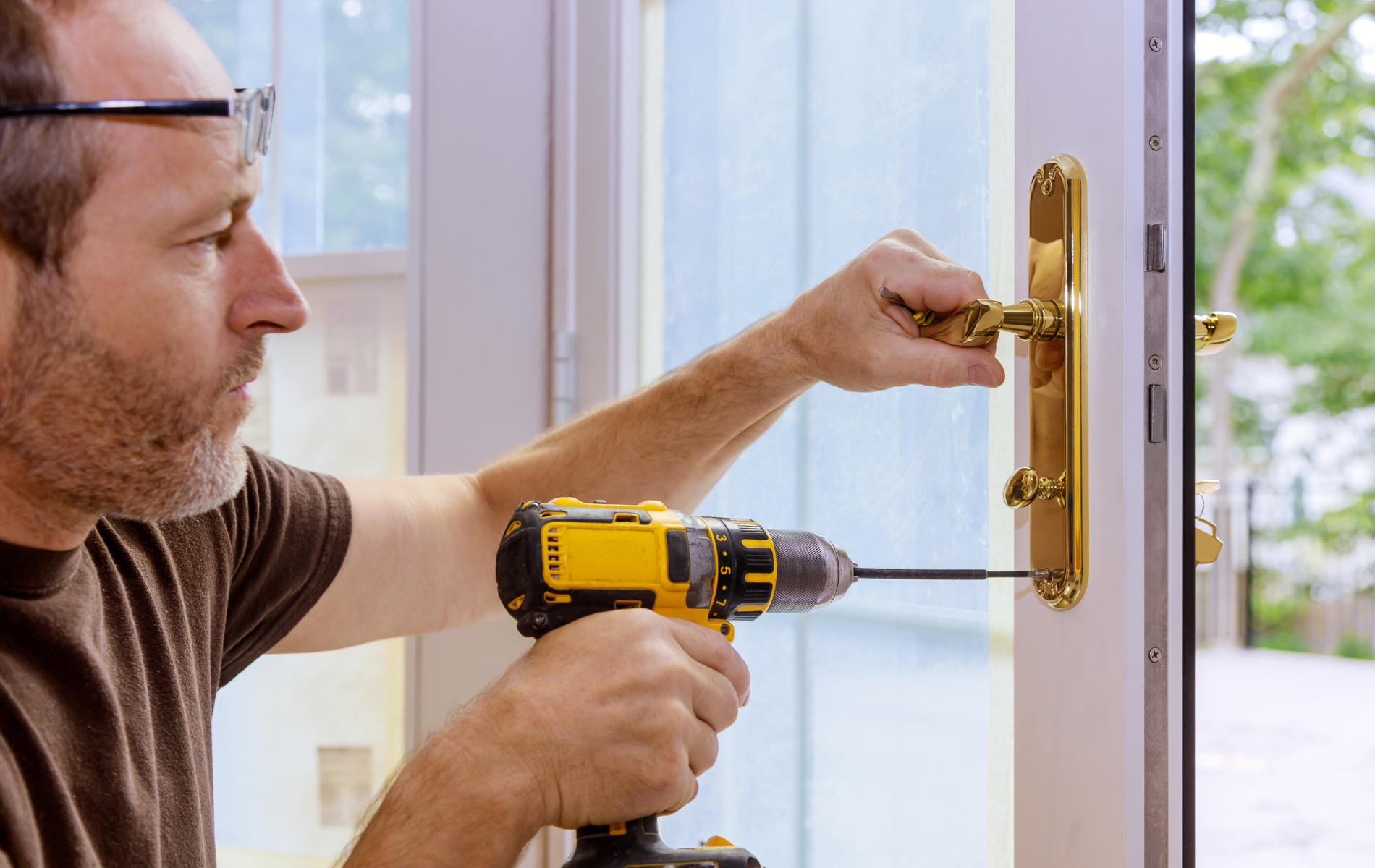 Person uses a power drill on a door handle in a doorway.