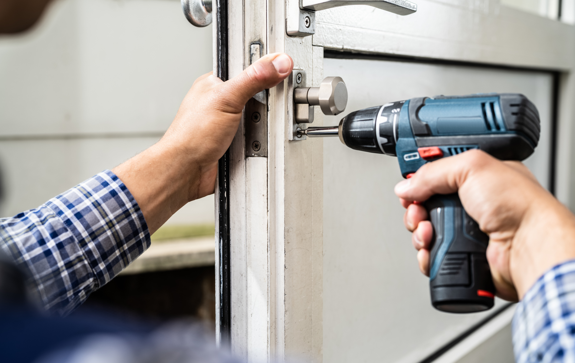 Person using a drill to install hardware on a white door frame.