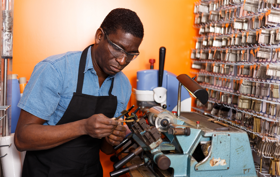 A person making a key with a key-cutting machine in a shop.