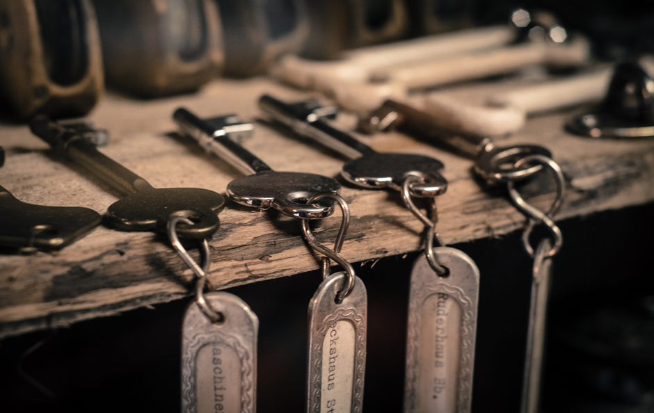 Antique keys hanging on a wooden shelf, each with a metal tag.