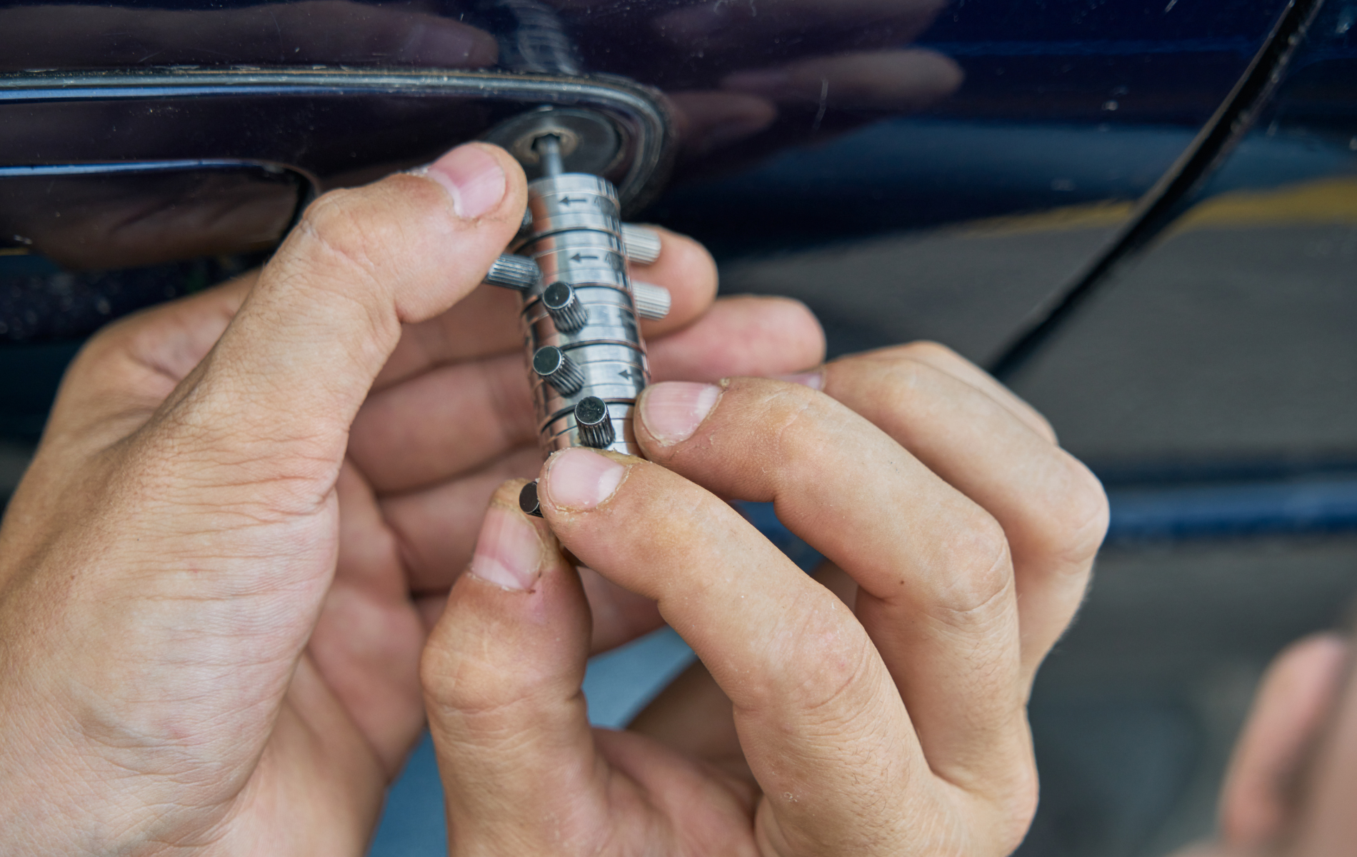 Hands removing the lock cylinder from a blue car door.