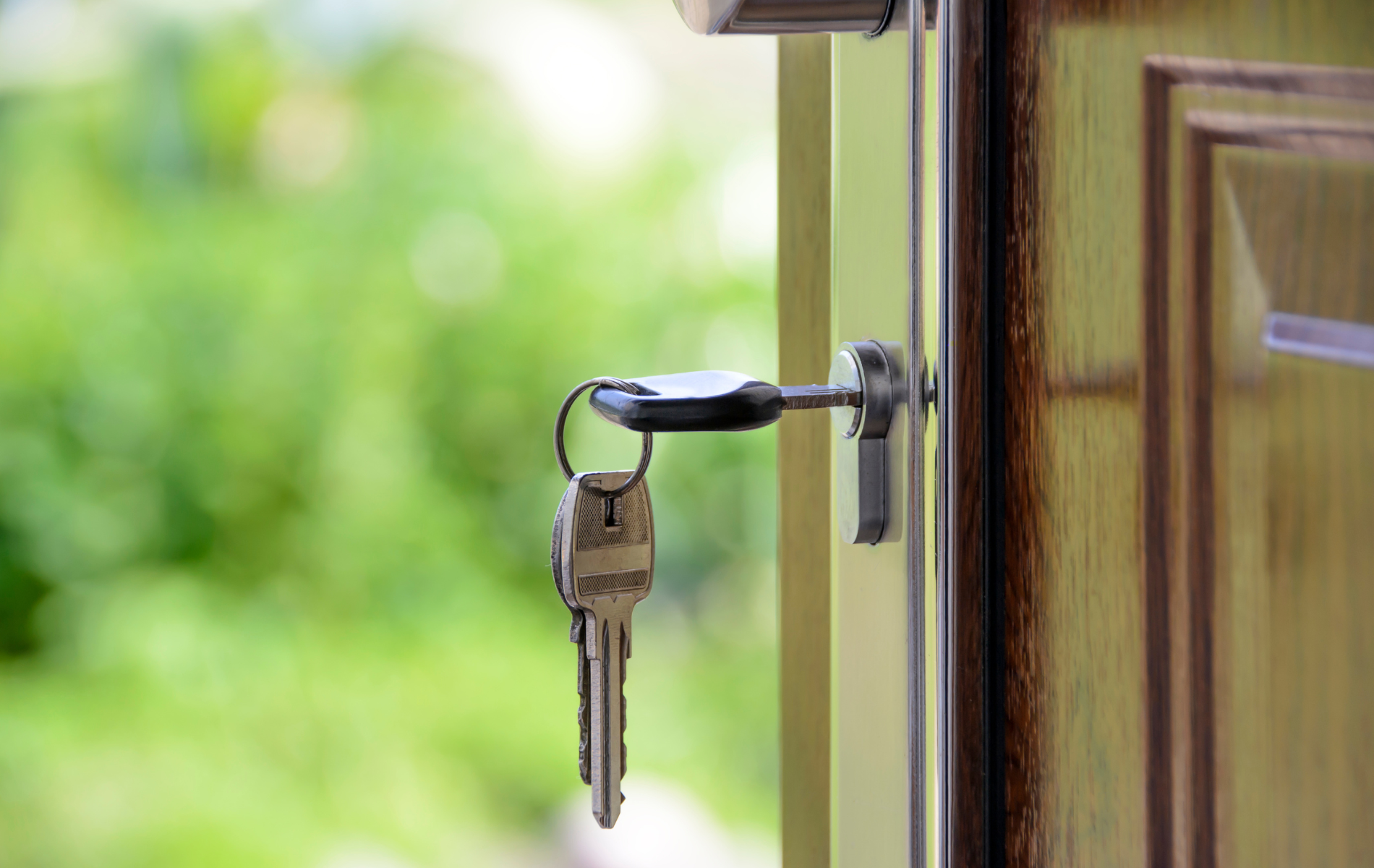 Door ajar with key in the lock, a ring with keys hangs. Green blurred background.
