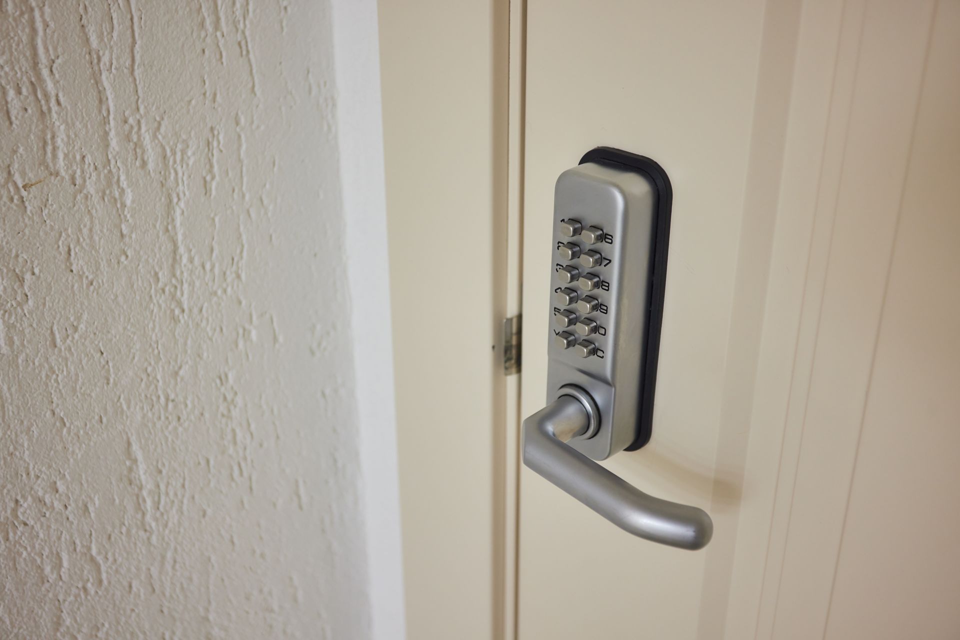 A door with a silver keypad lock and handle is set in a light-colored frame.