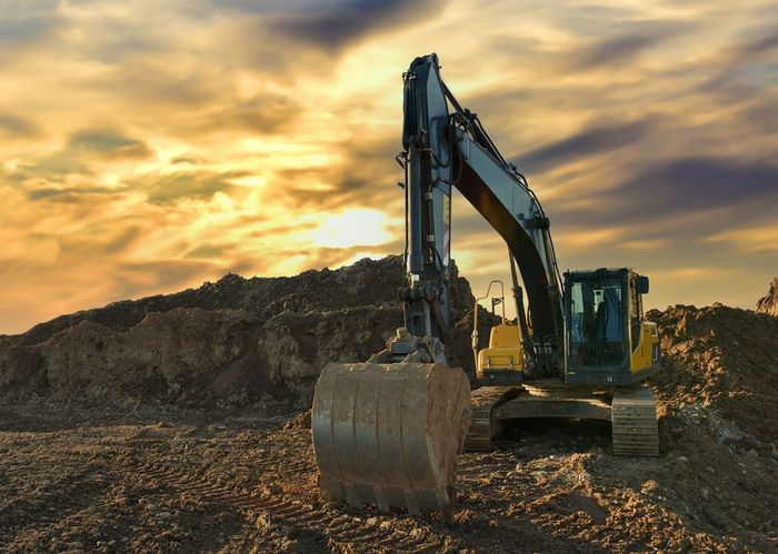 An excavator is sitting on top of a pile of dirt.