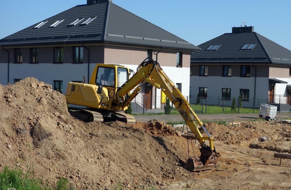 A yellow excavator is digging a hole in the dirt in front of a house.