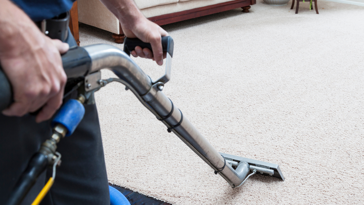 A man is using a vacuum cleaner to clean a carpet in a living room.