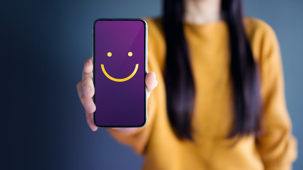 A woman is holding a cell phone with a smiley face on it.