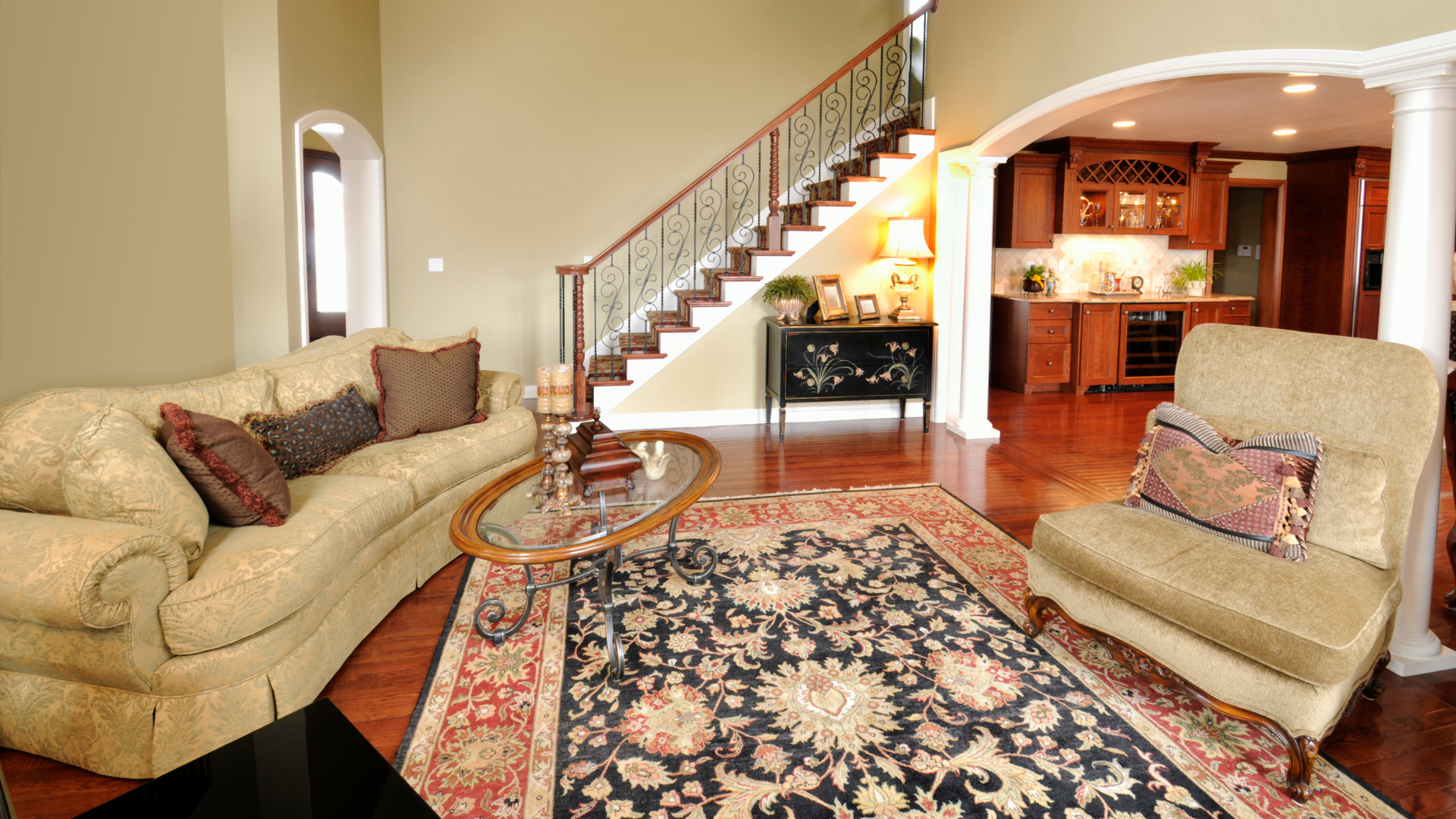 A living room with a couch , chair , coffee table , rug and stairs.