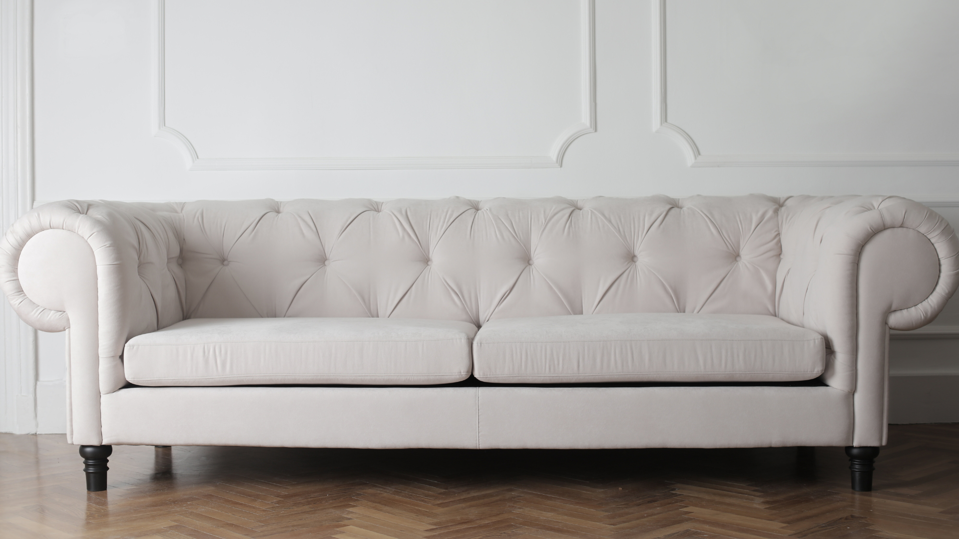 A white couch is sitting on a wooden floor in front of a white wall.