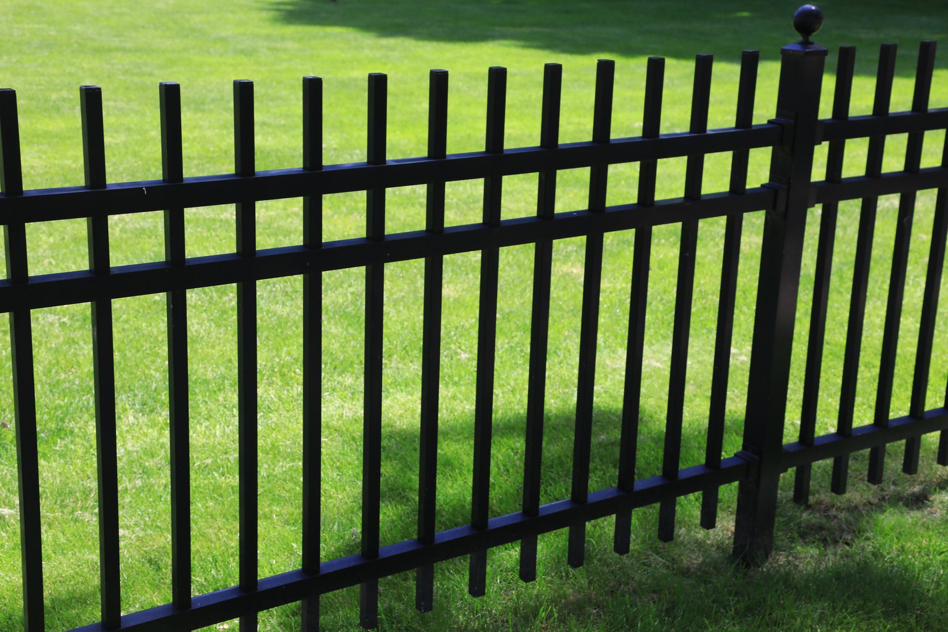 Black metal fence with vertical bars on green grass.
