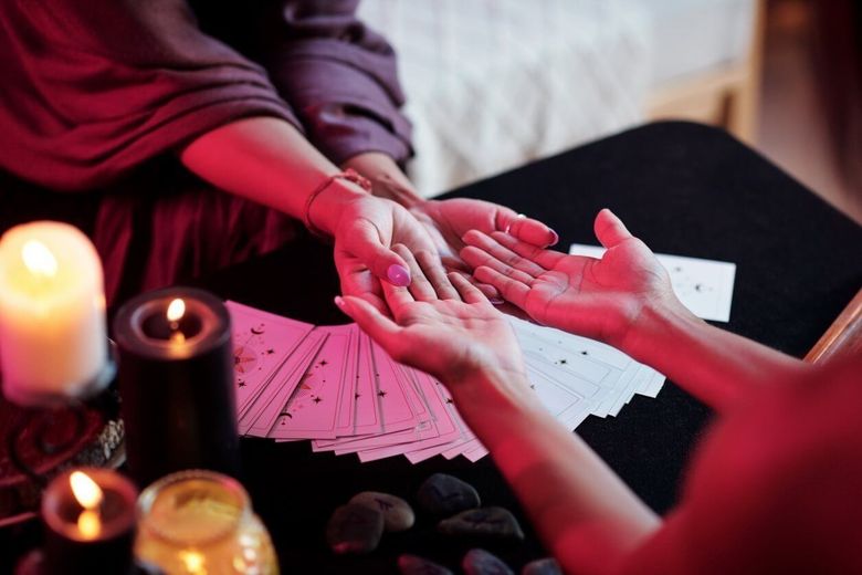 A woman is holding another woman 's hand while sitting at a table with tarot cards and candles.