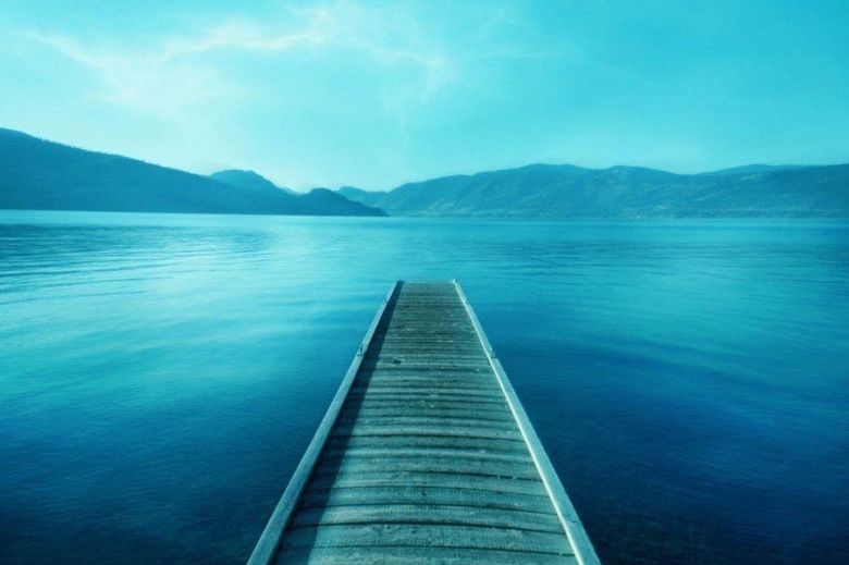 A wooden pier leading into a large body of water with mountains in the background.