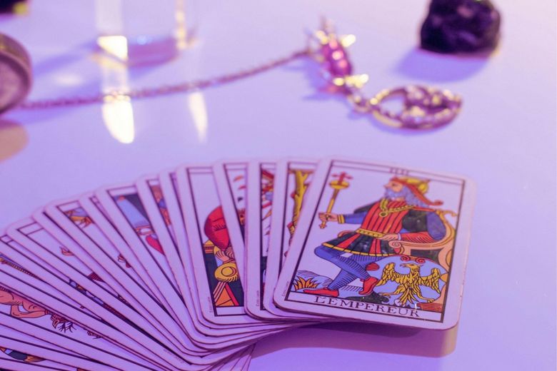 A deck of tarot cards on a table with a pendulum in the background