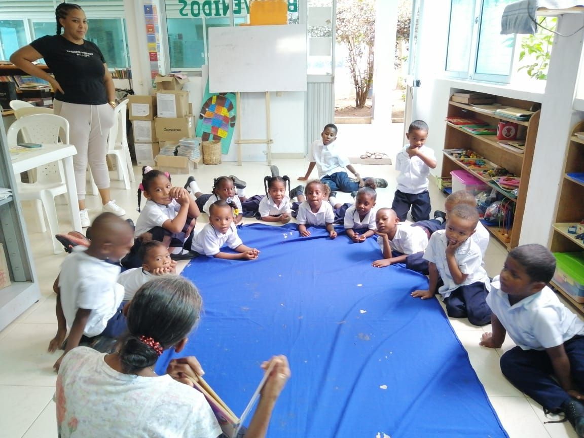 A group of students sitting around a blue mat getting ready to play an interactive game. 