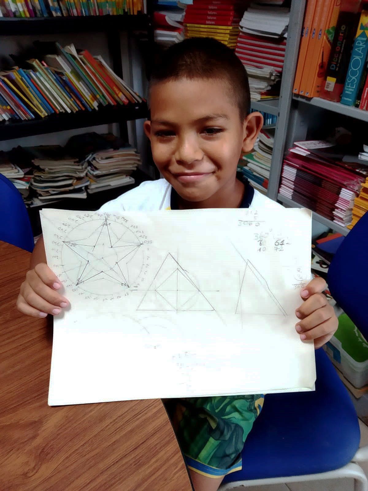 A young boy student holding up a paper drawing of a star with math angle calculations. 