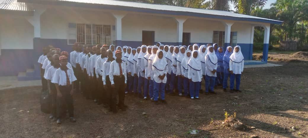 89 Girls and boys attending Kpatobu School standing in 6 rows in front of the school.