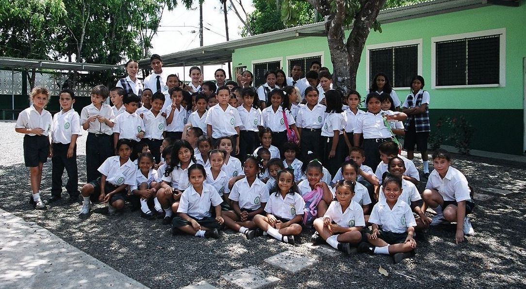 A large group of children are posing for a picture in front of a green building.