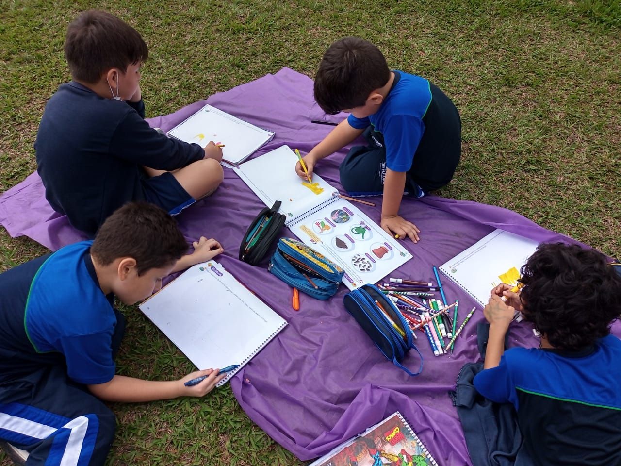 Four young boys sitting outside together creating art with different marker colors. 