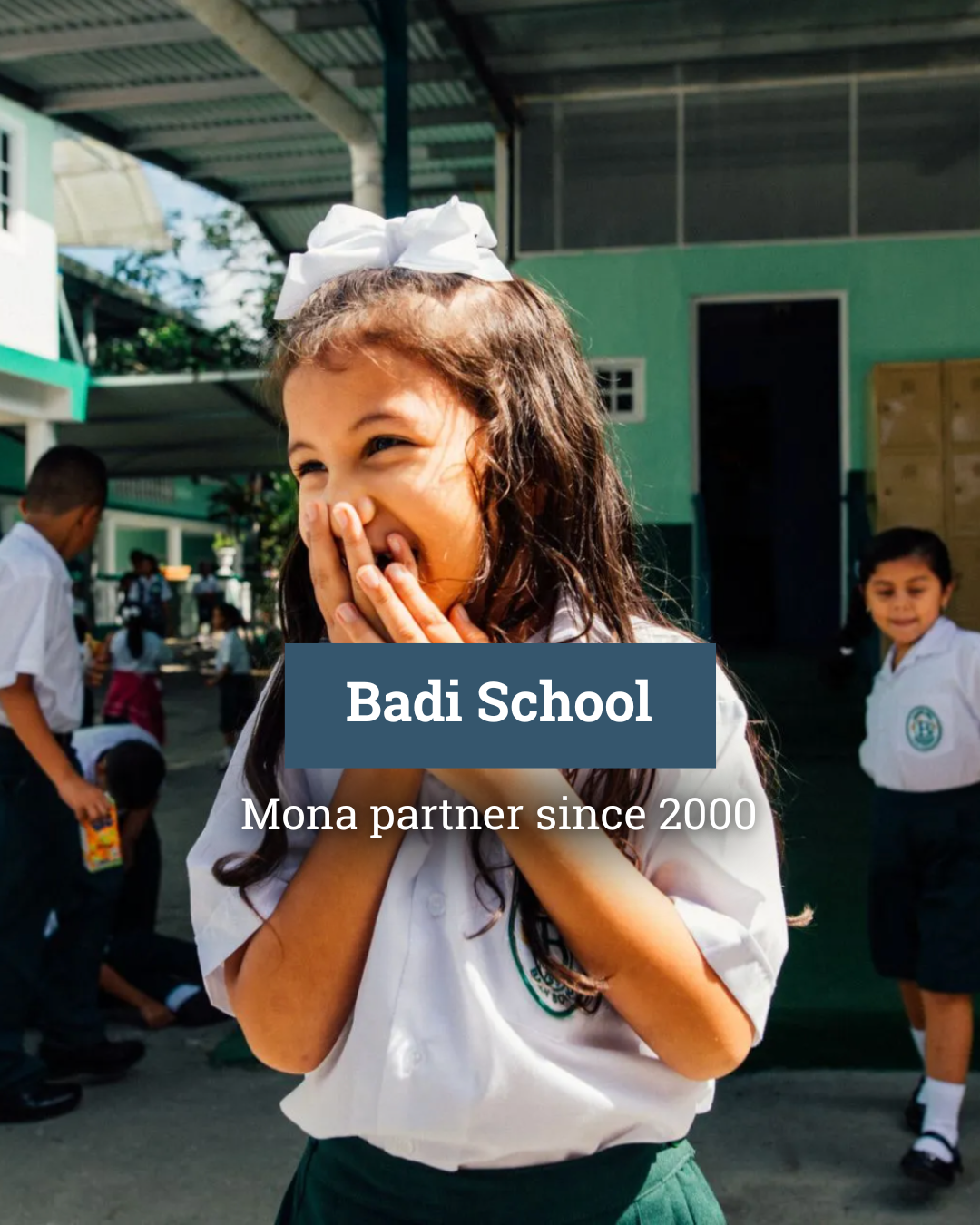 A little girl is covering her mouth with her hands in a school yard.