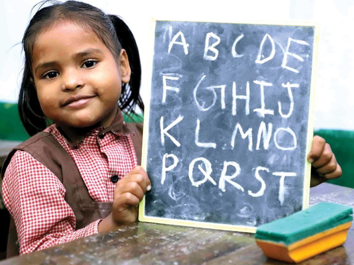 A young girl holding up a chalk board where she hand wrote the alphabet at Study Hall Educational Foundation, India.