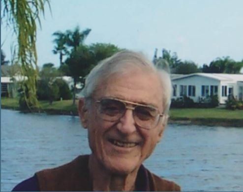 A man wearing glasses is smiling in front of a body of water