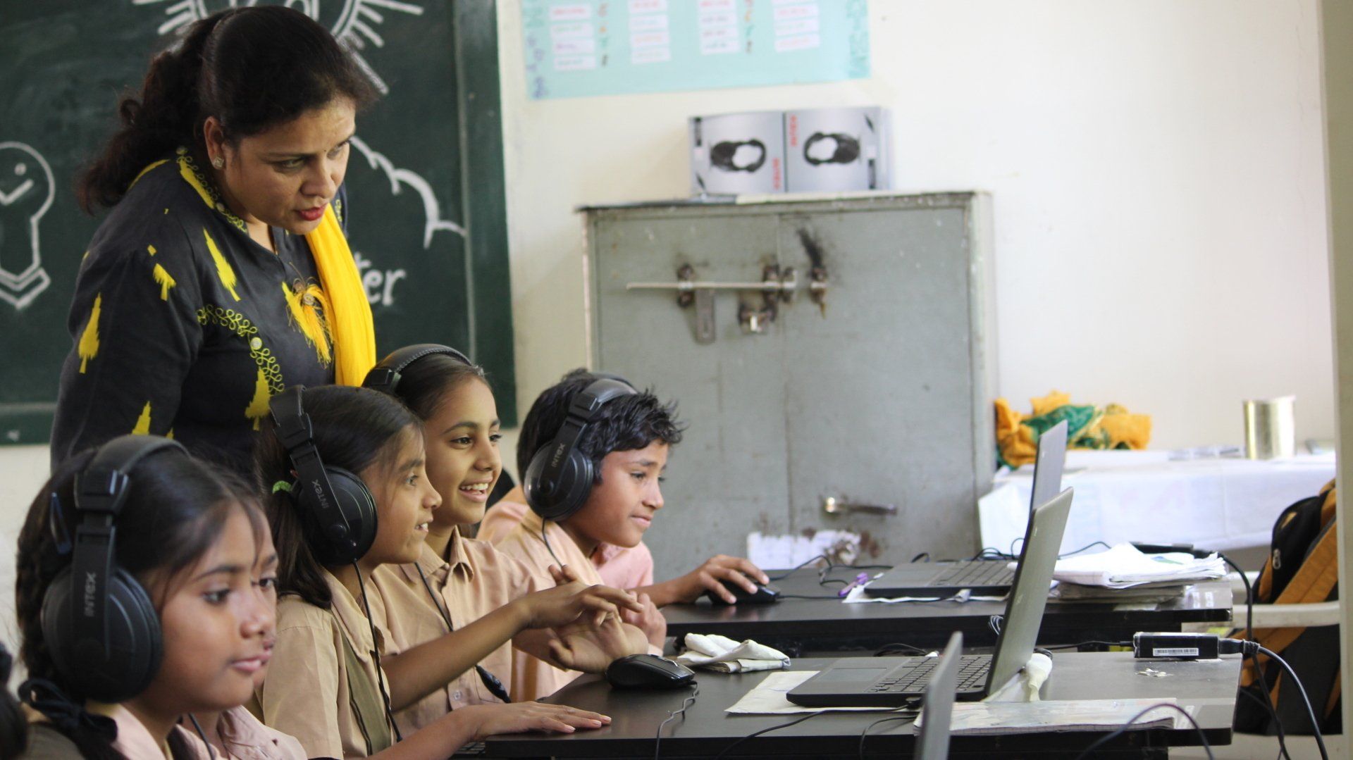 Three young students smiling, working on a computer with their teacher. 