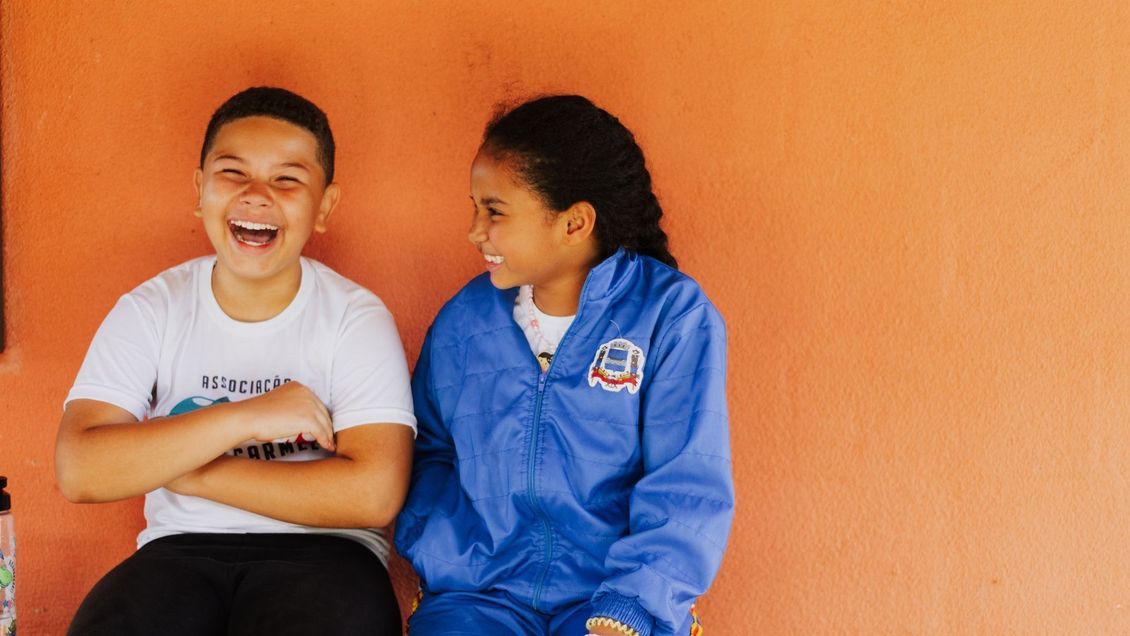 A boy and a girl are sitting next to each other and laughing.