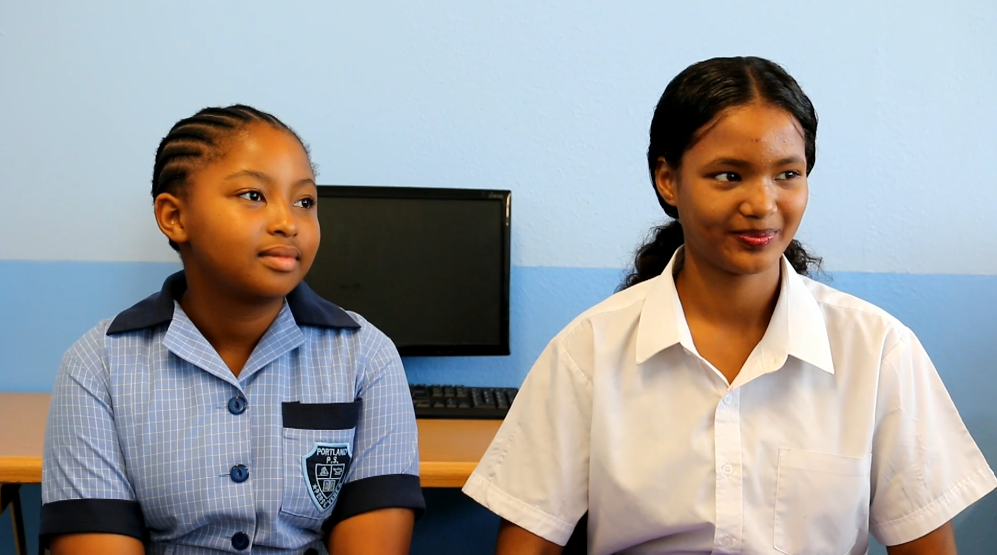 Two girls are sitting next to each other in front of a computer.