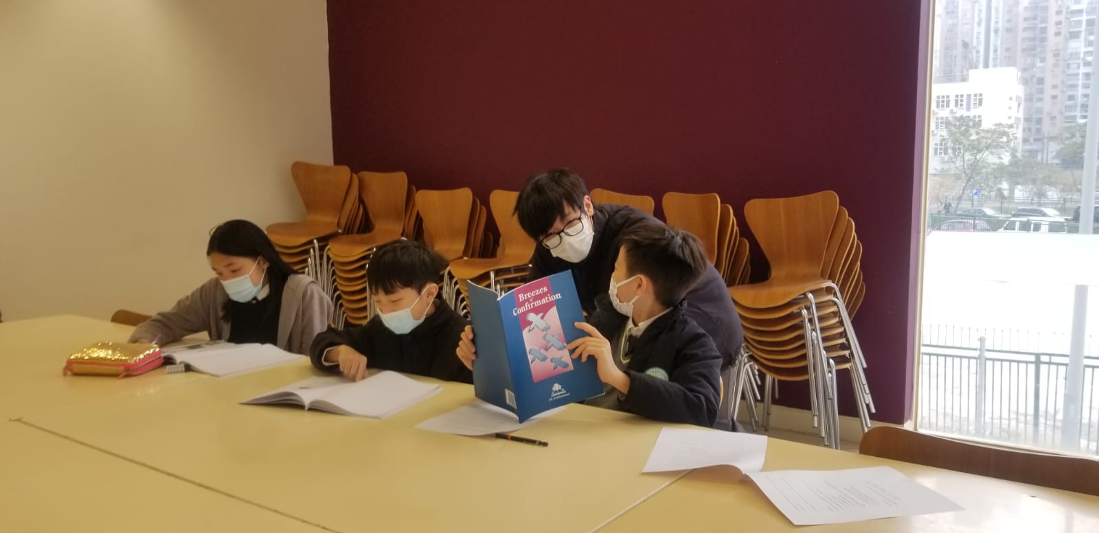 Three students reading a textbook while their teacher helps one of them. 