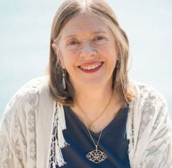 A woman wearing a necklace and earrings is smiling for the camera.