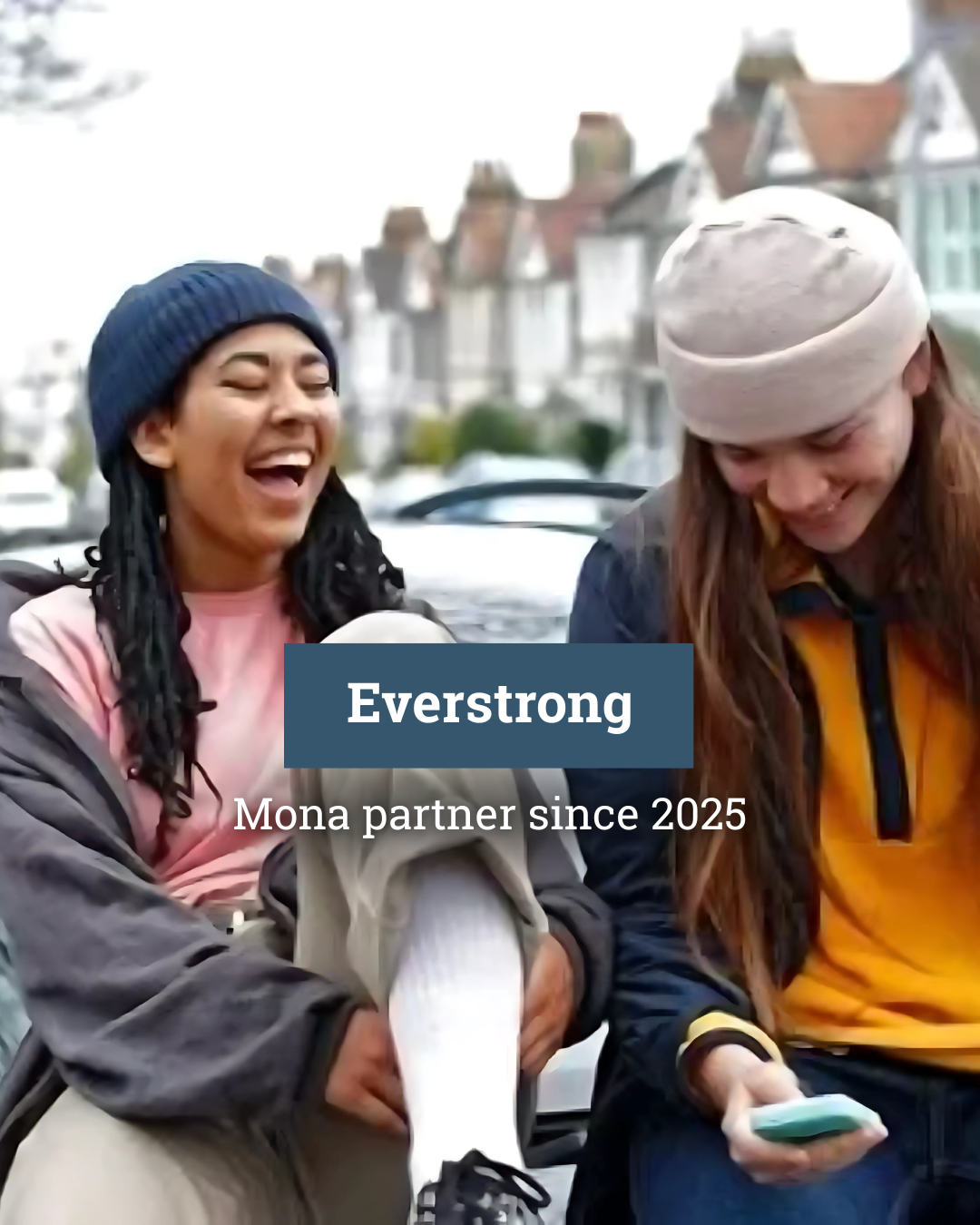 Two young women are sitting on the hood of a car.