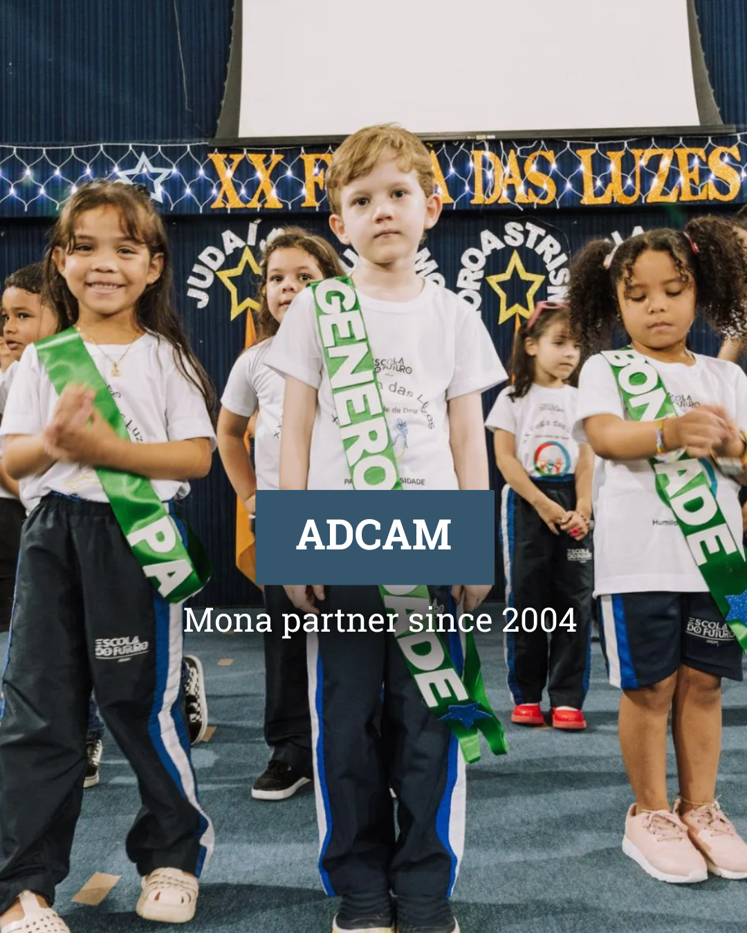 A group of children are standing in front of a stage holding sashes that say centrosidade