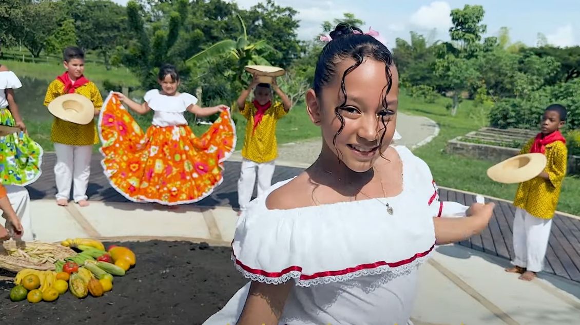 A girl in a white dress is dancing in front of a group of children.