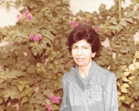 A woman is standing in front of a bush with pink flowers.