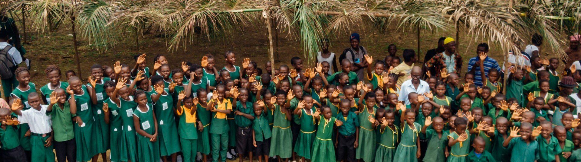 A large group of students at Programme for Children, Sierra Leone, smiling and waving. 