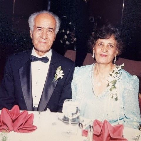 A man in a tuxedo and a woman in a blue dress are sitting at a table