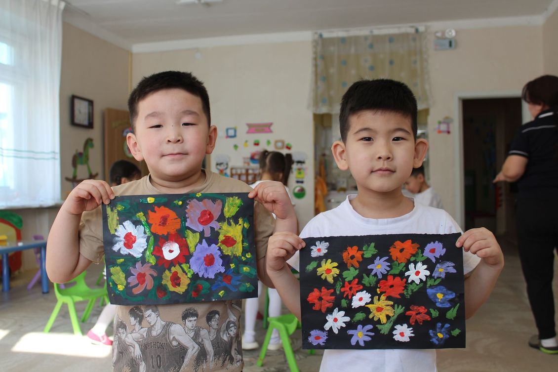 Two young boys are holding up a painting of flowers.