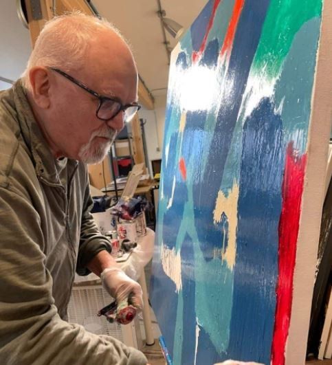 A man with glasses is painting on a large canvas