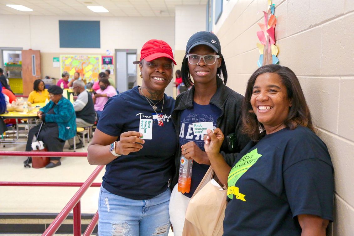 Three women are posing for a picture in a school cafeteria.
