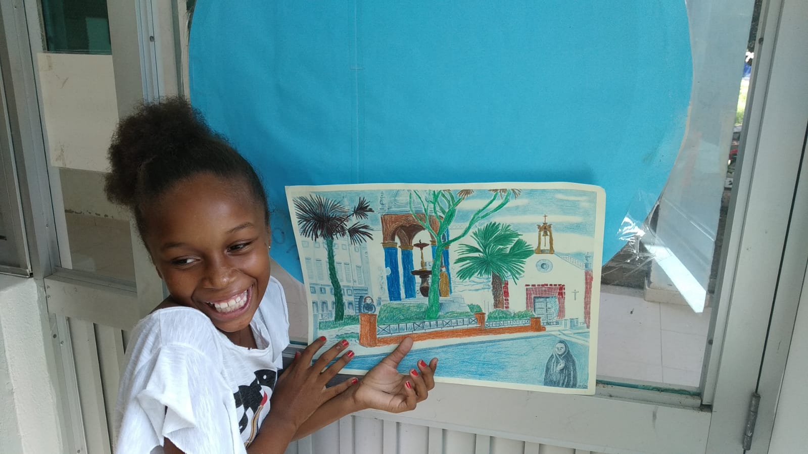 A young girl student holding up an art piece she made. 
