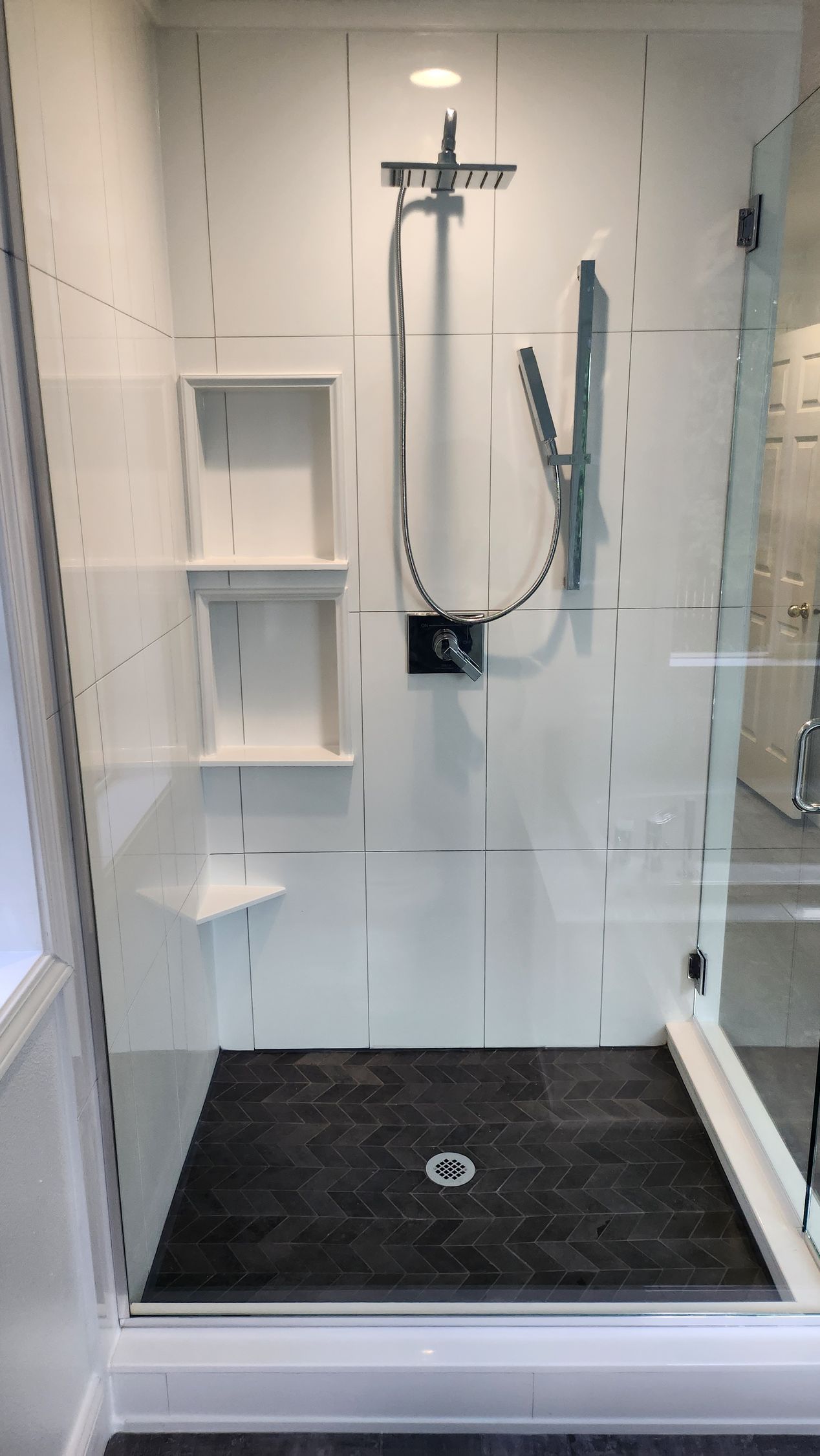 A bathroom with a walk in shower with a black tile floor.