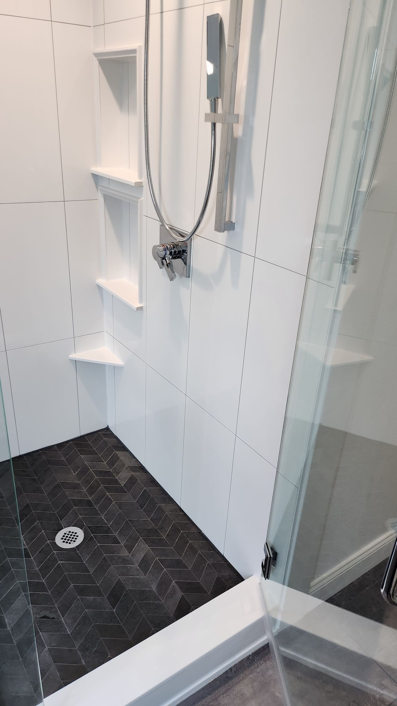 A shower with a black tile floor and a shower head.