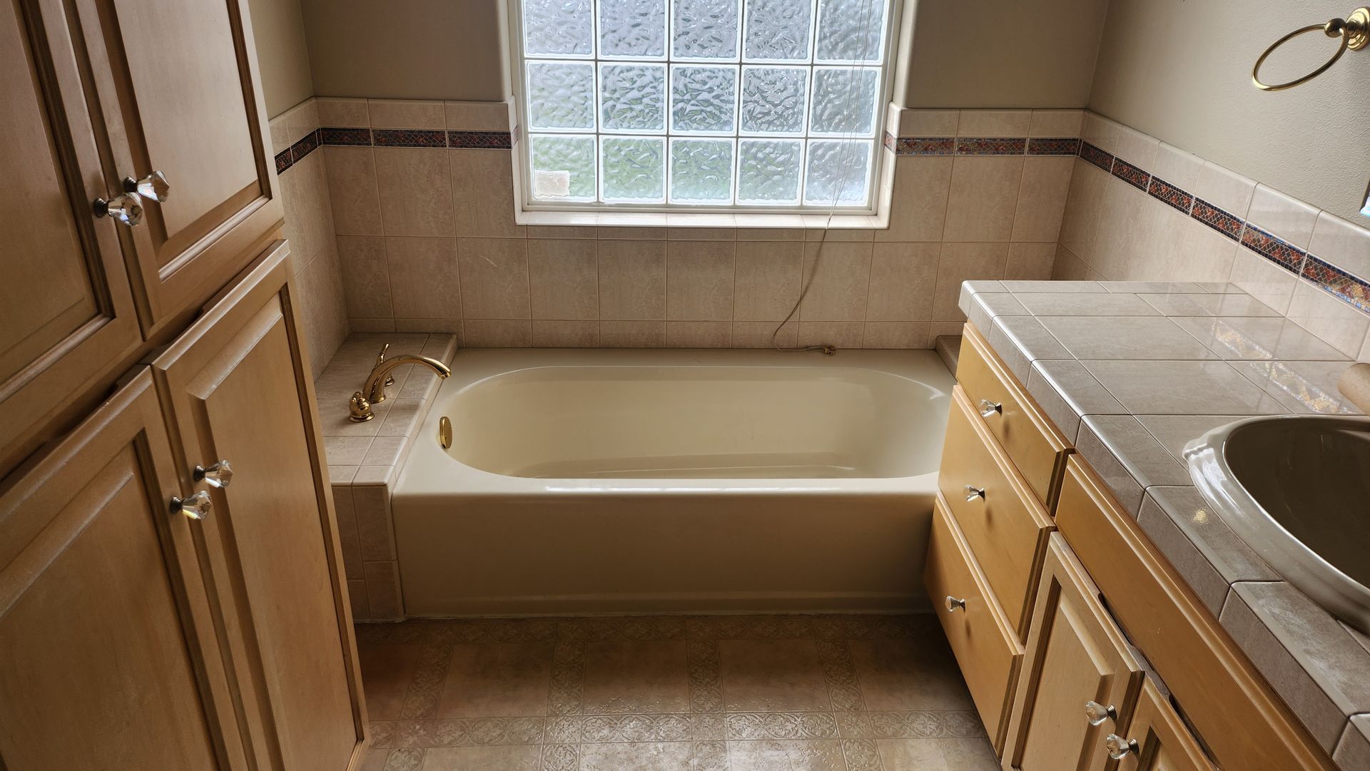 A bathroom with a tub , sink , cabinets and a window
