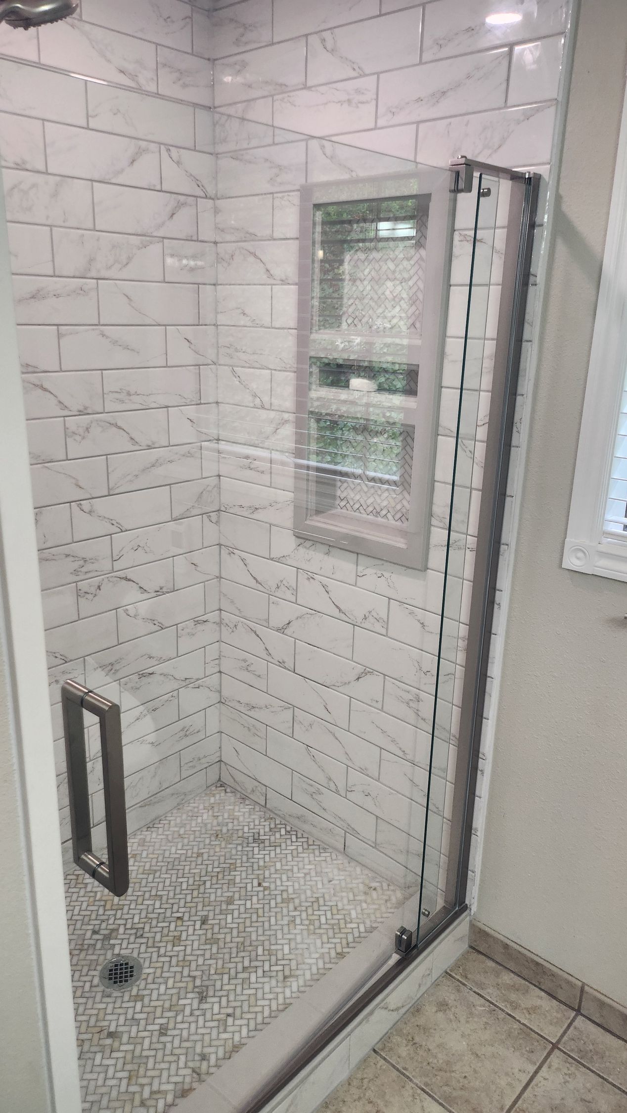 A bathroom with a walk in shower with white tiles and a glass door.