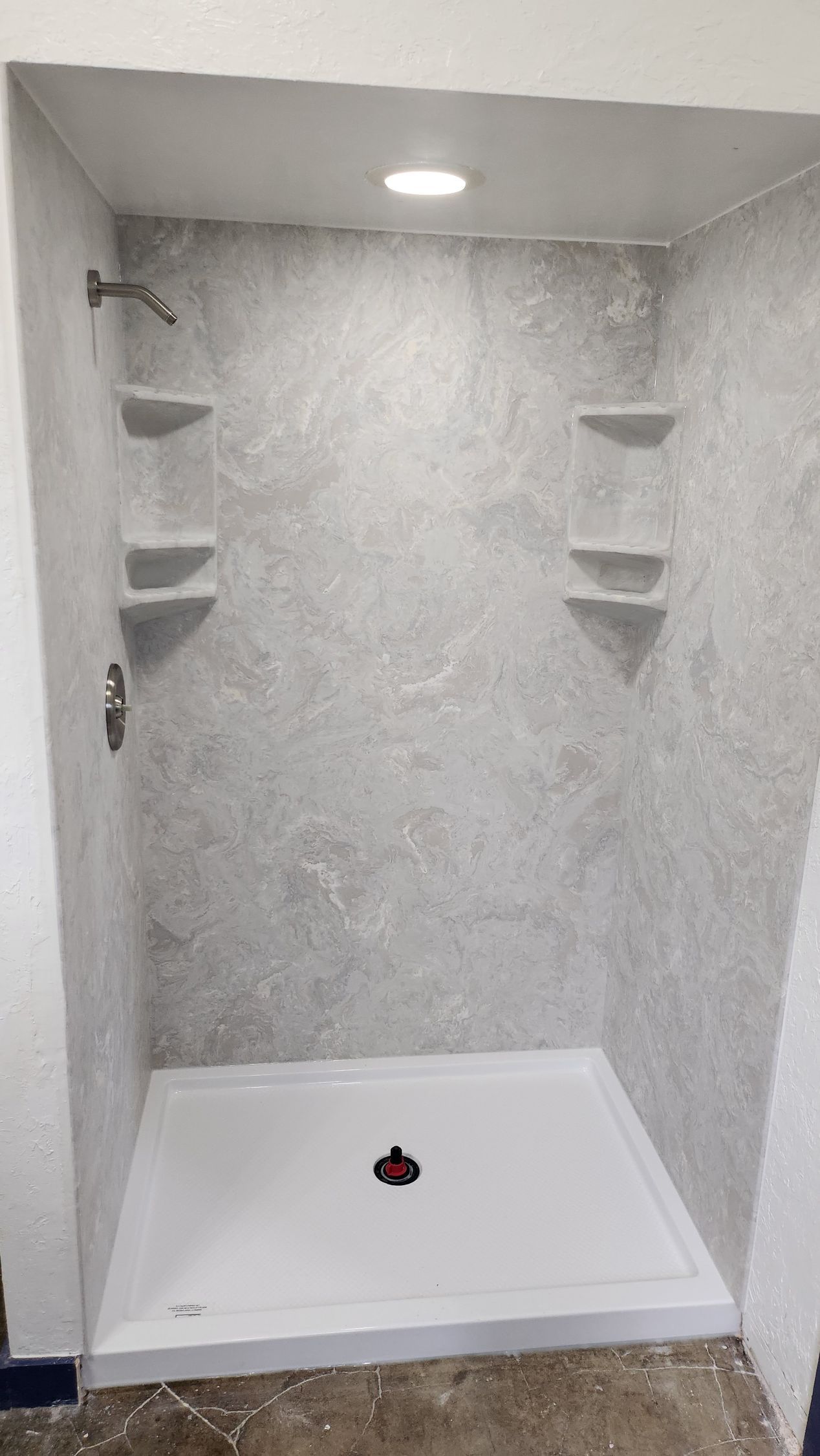 A shower stall with a shower head and shelves in a bathroom.