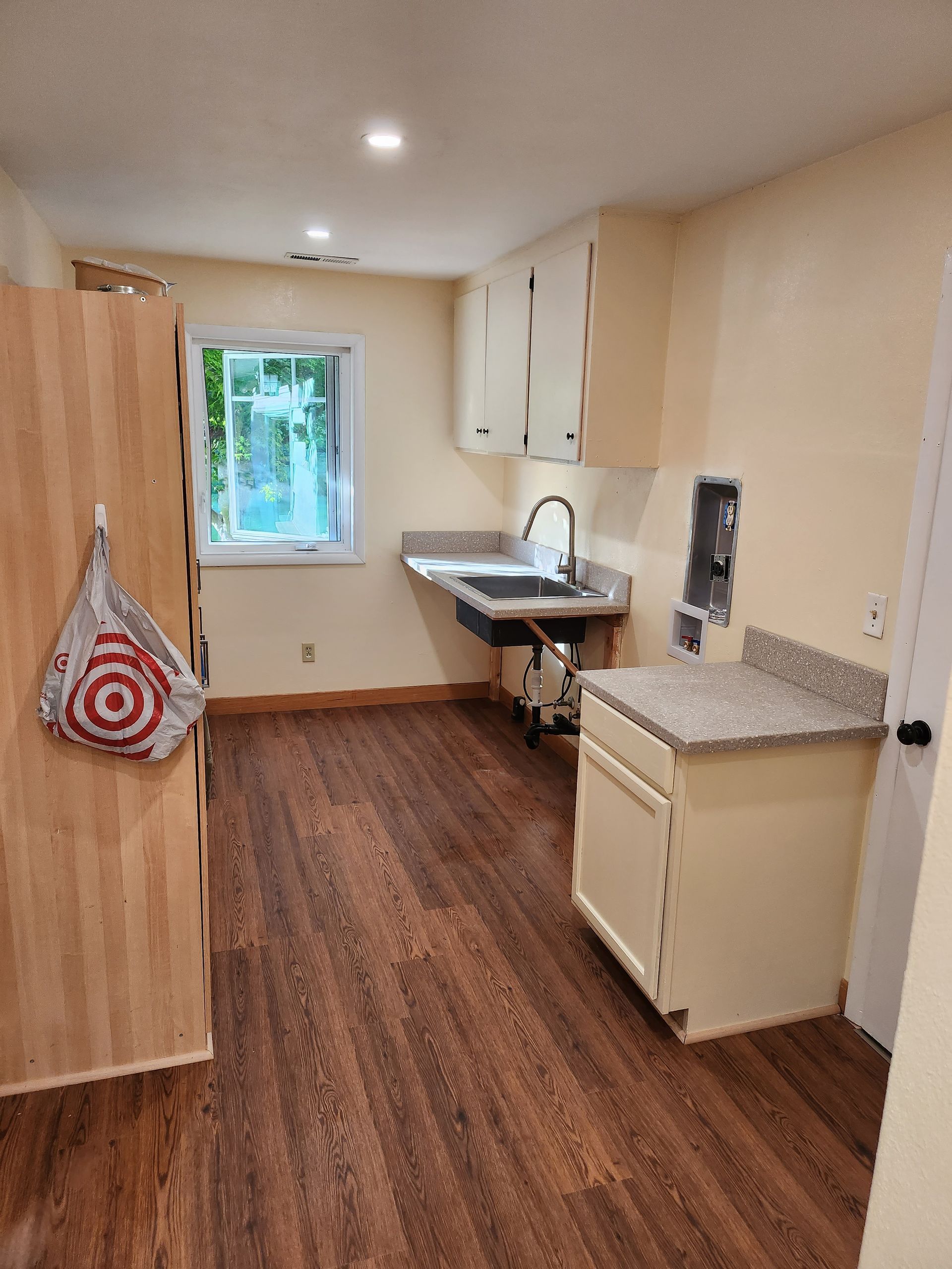 A laundry room with hardwood floors and white cabinets