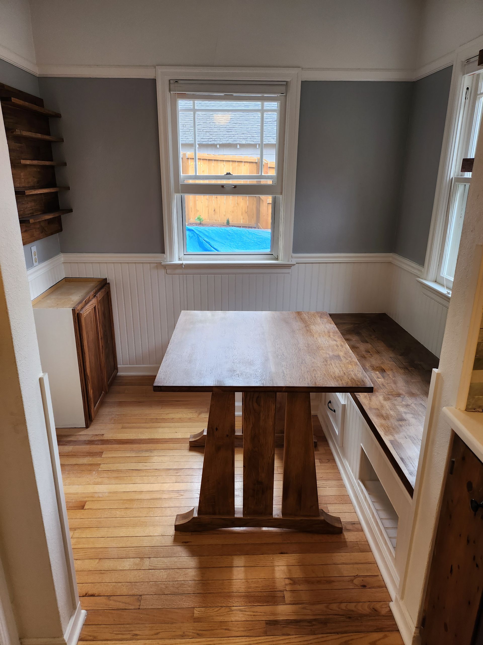 A wooden table with a bench underneath it in a room with a window.
