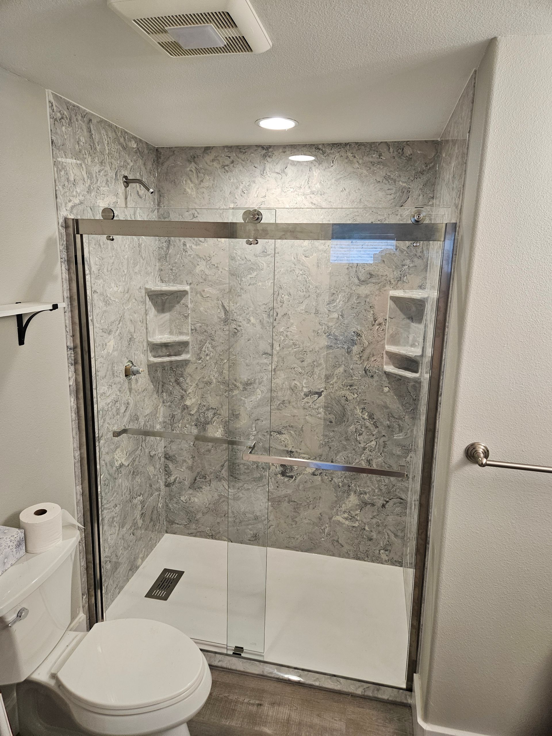 A bathroom with a toilet , shower and sliding glass door.