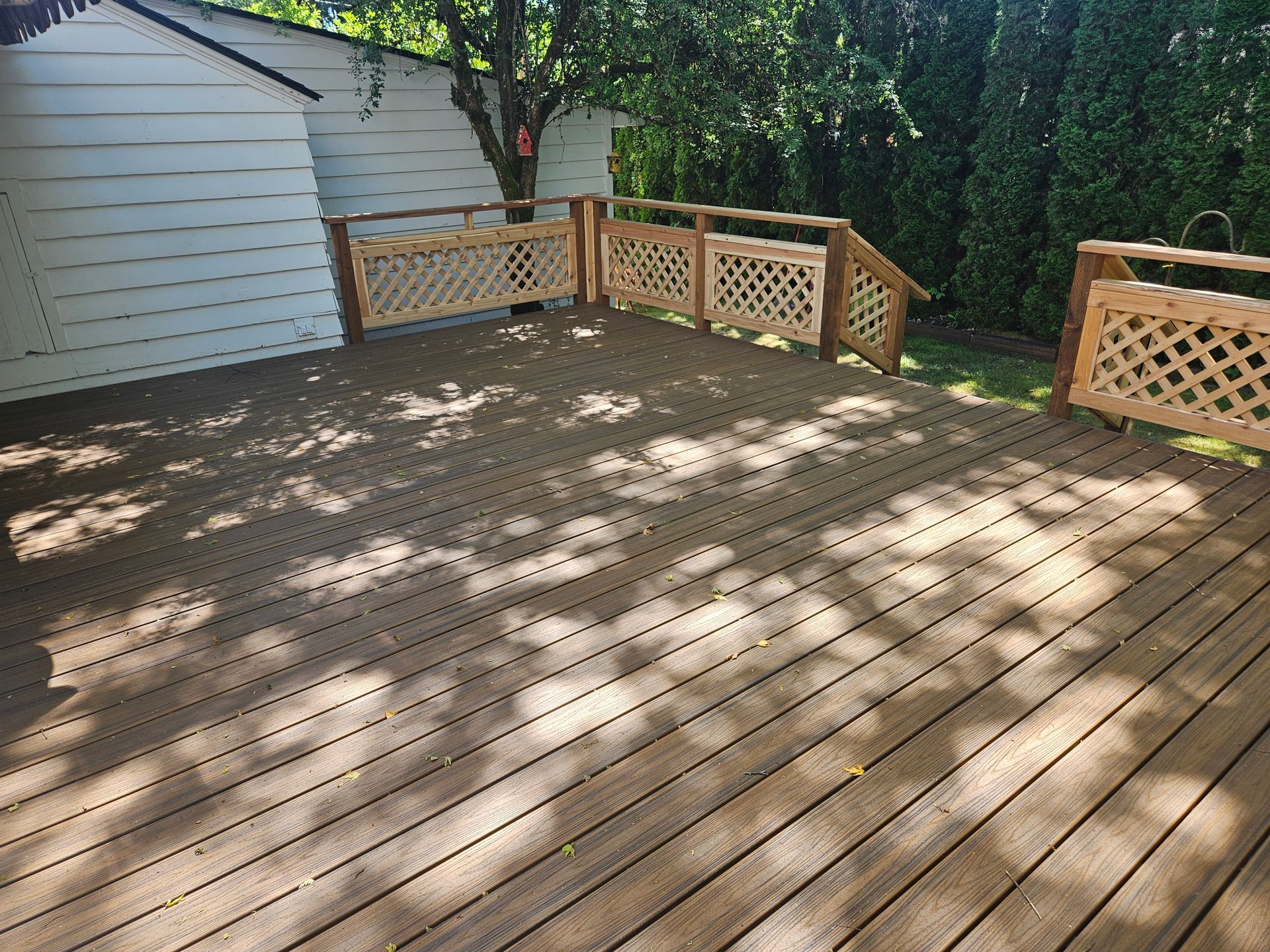 A wooden deck with a wooden railing and stairs in a backyard.
